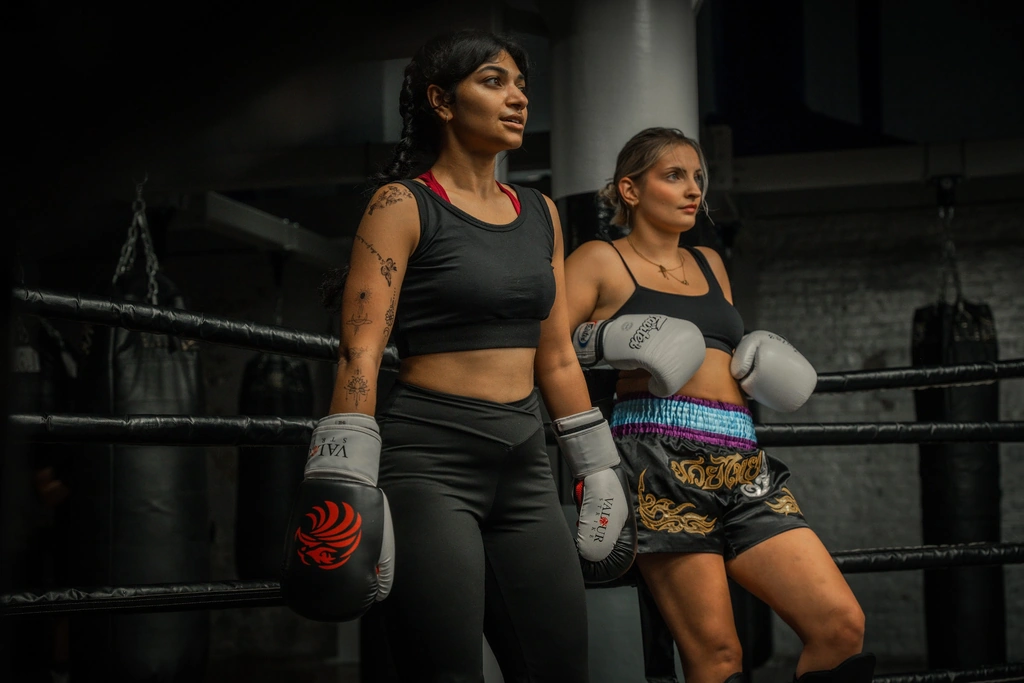 Two women in Muay Thai kit smiling in the ring at training
